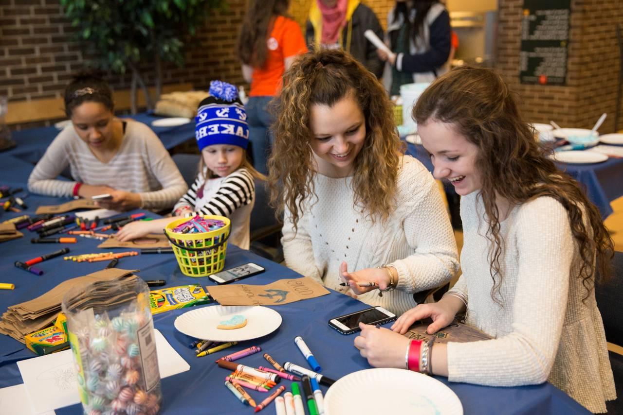 Two older female students making arts and crafts with a little girl